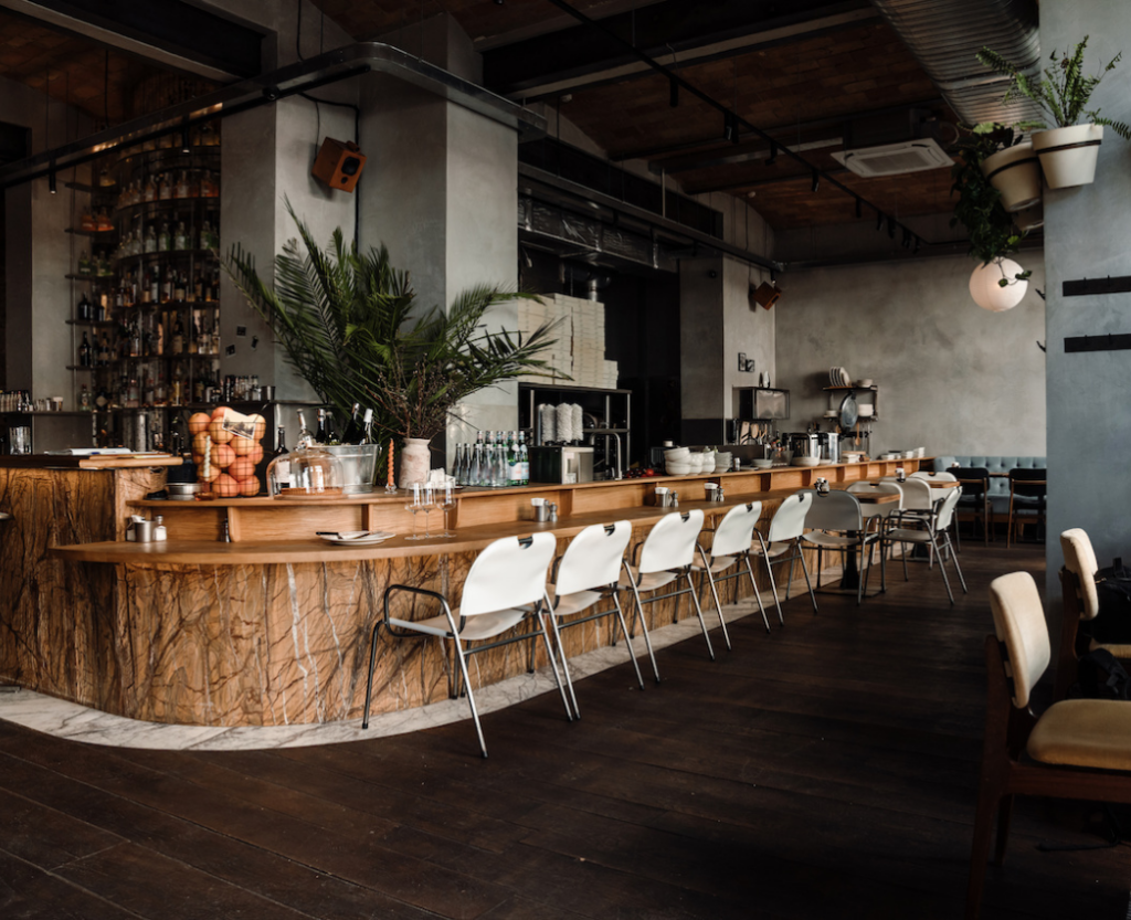 Contemporary restaurant interior featuring bar seating, wood tables, stylish chairs, and open shelving—highlighting modern FF&E for dining and hospitality spaces.